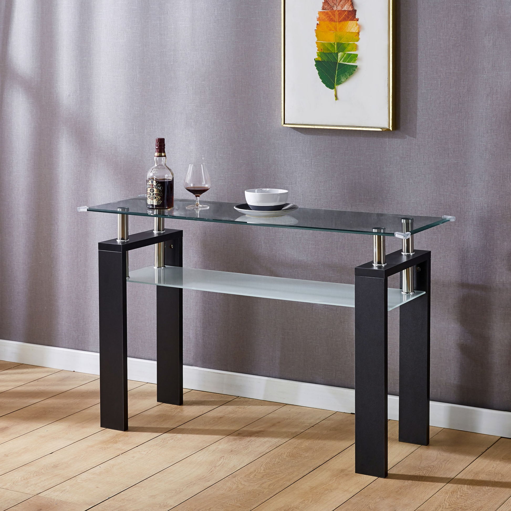 A Clear Glass Top Side Table, Modern Design For Home with black legs stands against a gray wall. On the table are a wine bottle, red wine glass, and white bowl. Above hangs a framed artwork featuring rainbow-colored feathers.