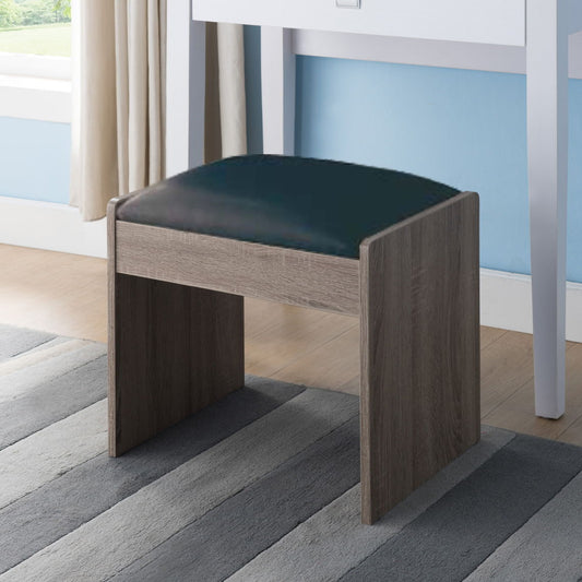A Vanity Cushioned Stool Chair Dark Brown with a black seat stands on a gray striped rug before a white desk, with a window and beige curtains in the background.