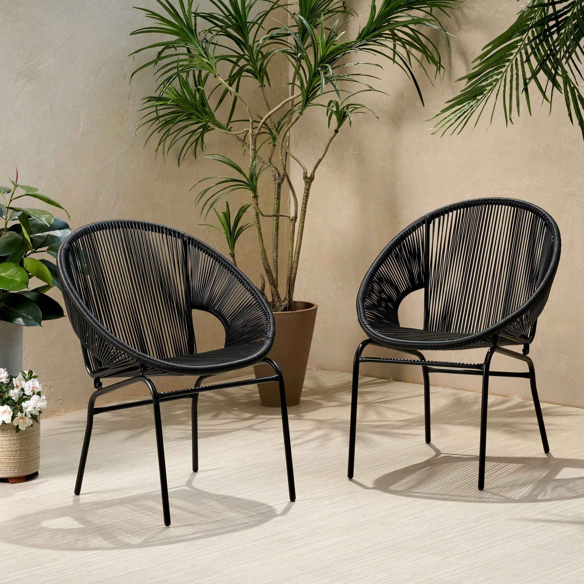 Two Nusa - Modern Chair Outdoor Seating pieces with open, circular black backs sit on a light floor. Potted green plants and a beige wall add to the minimalistic, inviting setting.