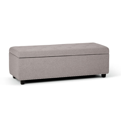 The Hamilton Upholstered Storage Ottoman features a rectangular light gray design with a padded, tufted lid and short black legs, shown against a white background.