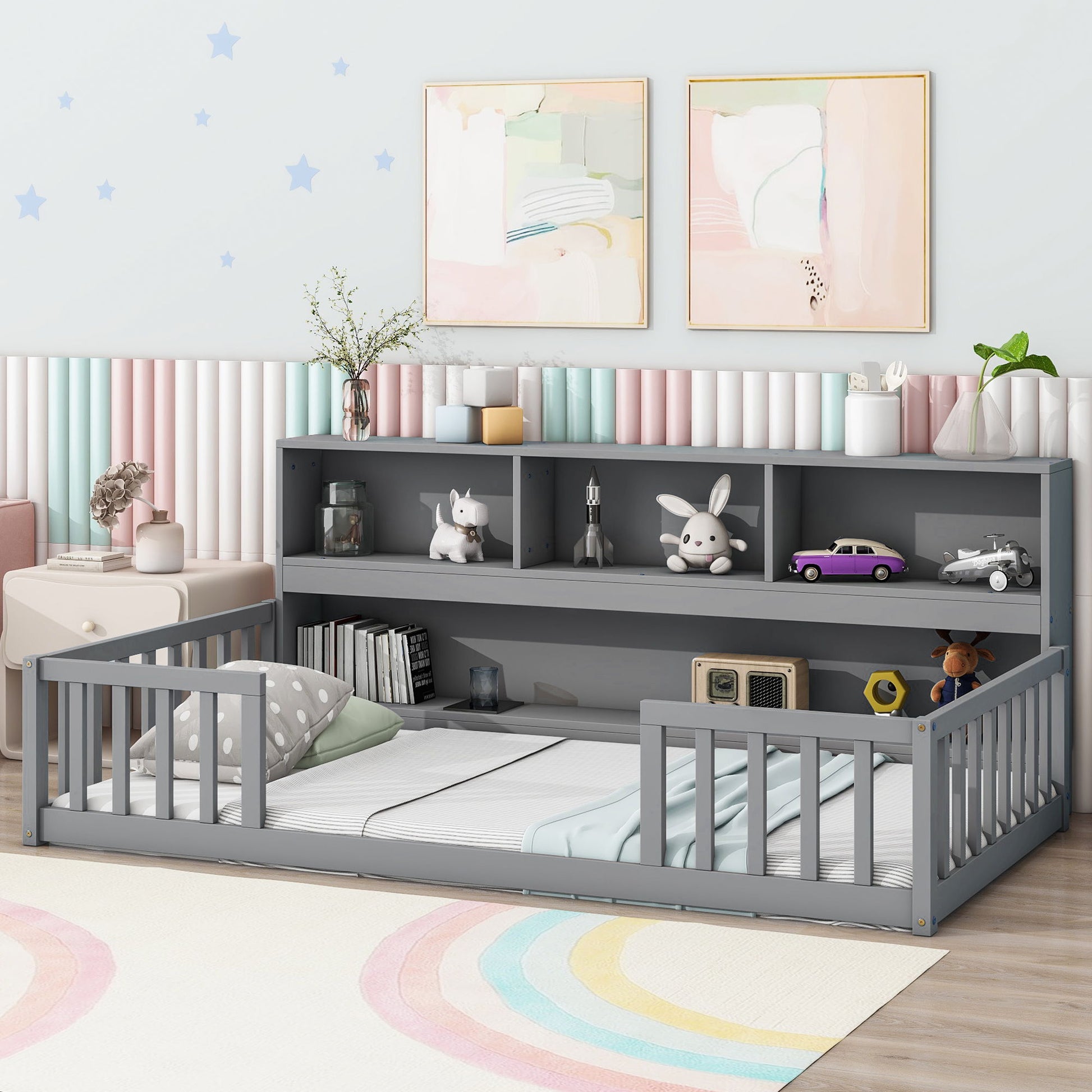 A Floor Bed With Bedside Bookcase, Shelves, and Guardrails is filled with toys and books, set in a pastel-themed room with wall art and a rainbow rug, creating a cozy and playful atmosphere.