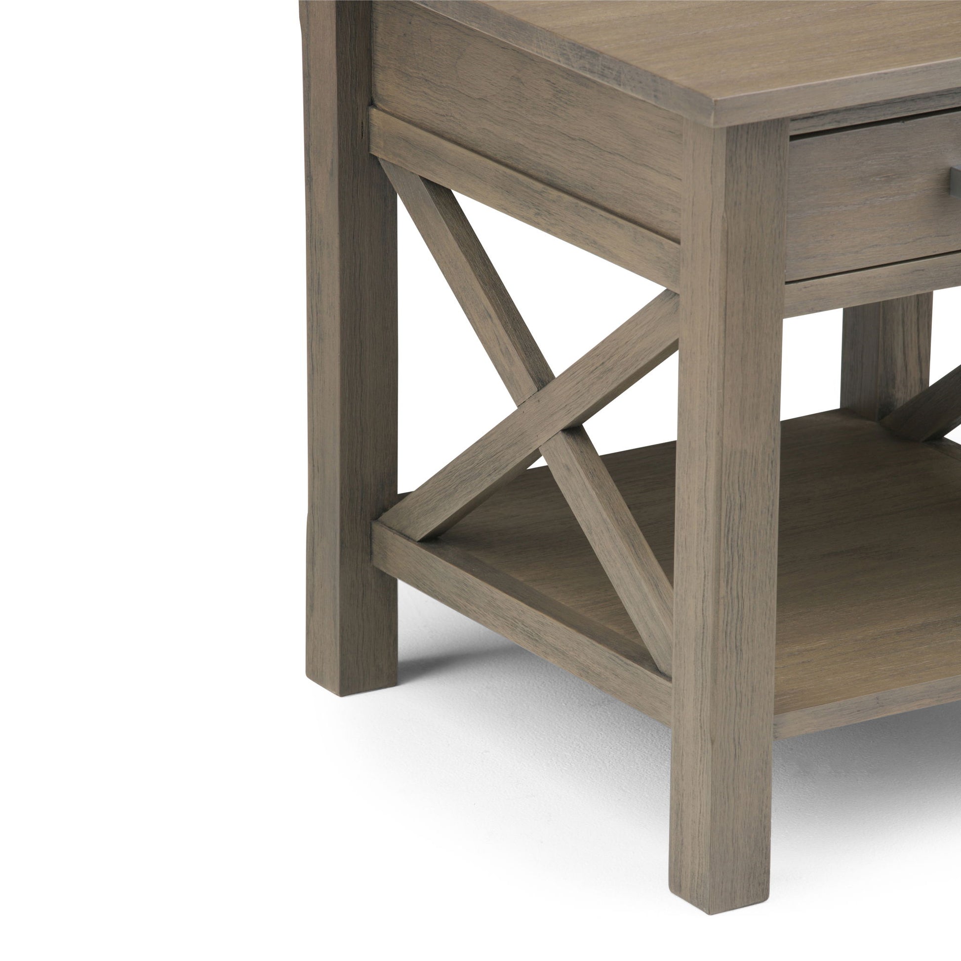 A close-up of the Kitchener - Handcrafted Table’s corner showcases its X-shaped side design, lower shelf, and partial drawer, all in a light brown wood finish.