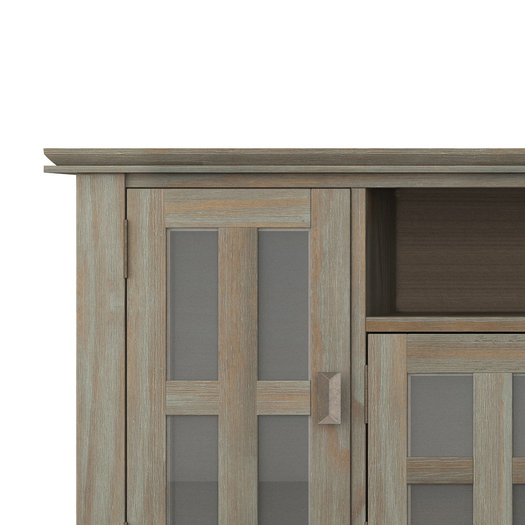 A close-up of the Artisan - TV Media Stand shows its weathered wood finish, glass-paneled doors with rectangular metallic handles, a rustic look, and an empty open shelf above the doors.