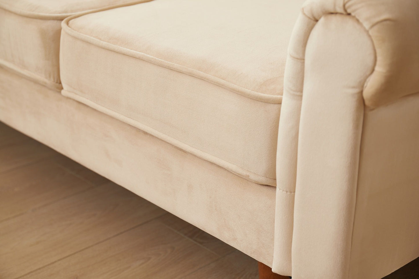 Close-up of the Graceful Design Plush Comfort Sofa, featuring beige upholstery, plush seat cushions, rounded armrest, and wooden legs on a wooden floor.