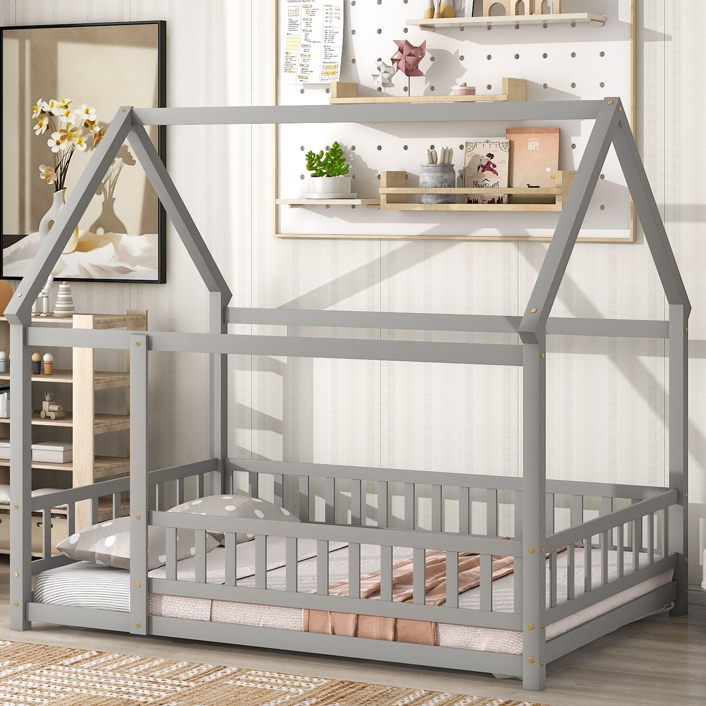 The room features a Floor Wooden Bed With House Roof Frame and Fence Guardrails, low to the floor with a pink-and-gray polka dot blanket, shelves with decor, a rug, cabinet, and soft natural light.
