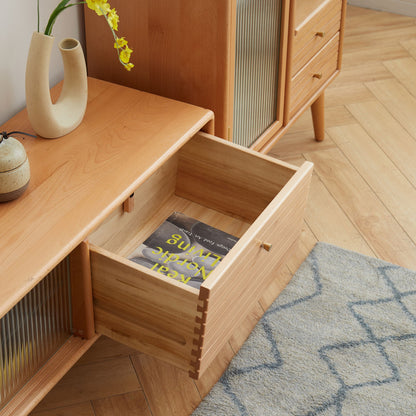 A TV Cabinet with Chinese Changhong glass doors and two drawer storage stands on a herringbone wood floor beside a geometric-patterned rug and decorative vases with a yellow flower. One drawer is open, revealing a book inside.