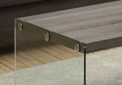 A close-up of the Coffee Table Rectangular For Living Room Clear Tempered Glass shows a wooden tabletop joined to a clear glass leg with three round metal fasteners, set on light hardwood flooring and a beige rug.