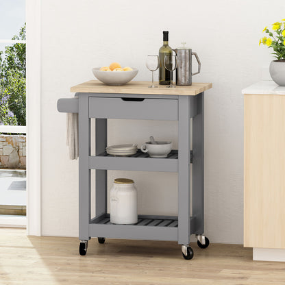 The Tattnall Kitchen Cart With Wheels, featuring a gray finish, wooden top, drawer, towel bar, and two shelves, holds kitchen essentials and is placed by a wall near a sunlit window.