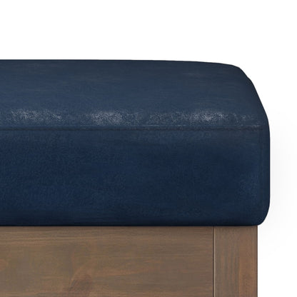 A close-up of the Milltown - Upholstered Ottoman Bench features its dark blue cushioned seat and wooden frame, highlighting corner and edge details against a white background.