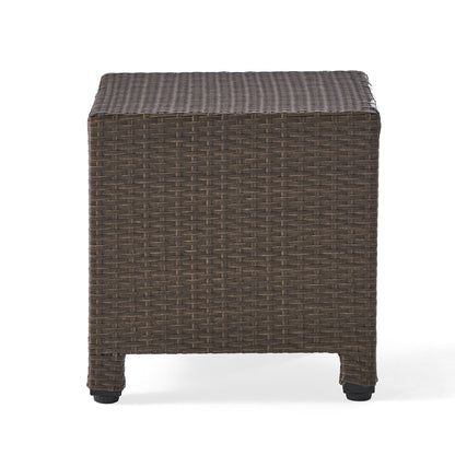 The Puerta Minimalist Style Accent Table features a square design with a flat top and short legs, crafted from brown woven rattan and shown against a white background.
