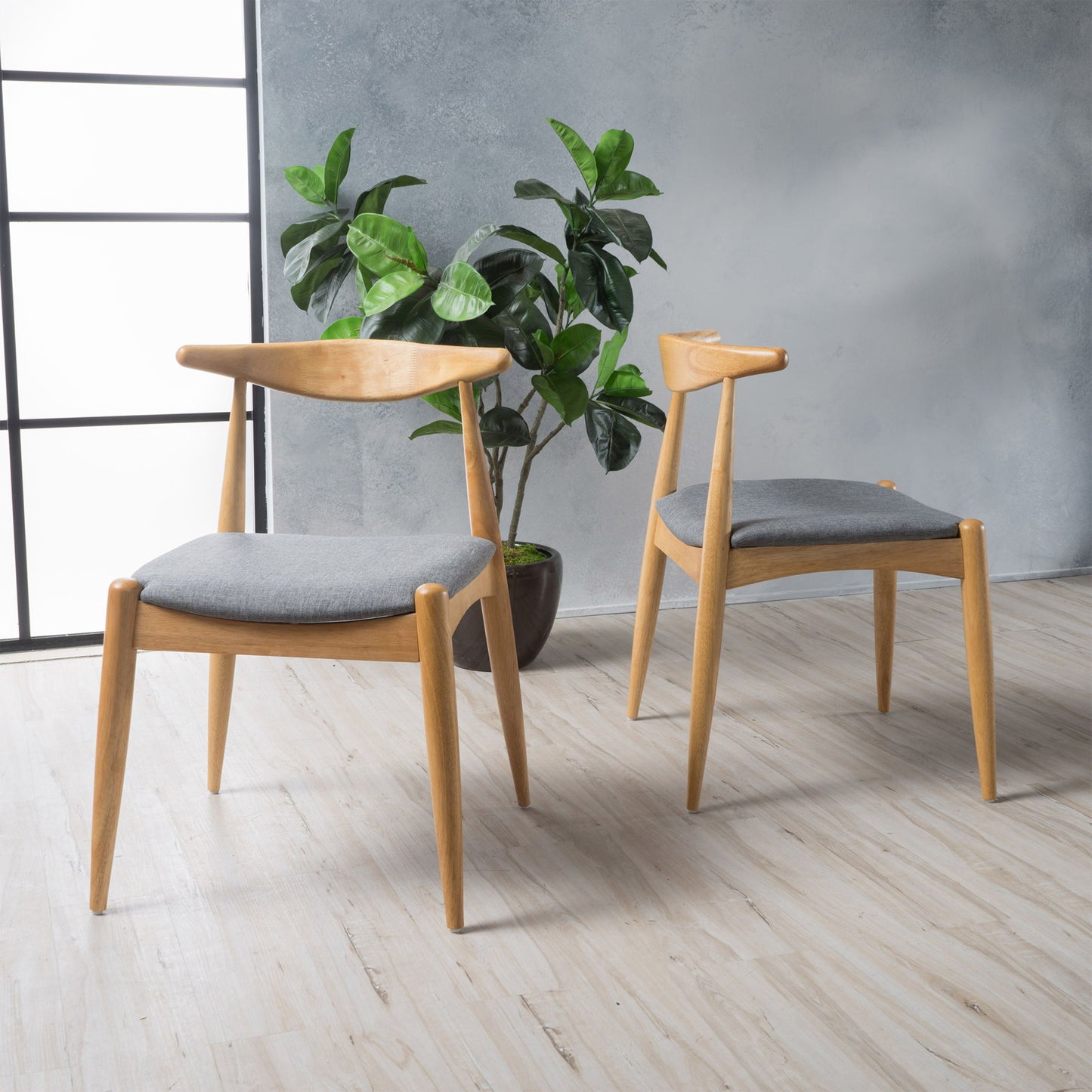 A set of two Candescent Dining Chairs with curved backs and wood frames, featuring gray cushions, sit on a light wood floor near a potted plant, against a gray textured wall and large window.