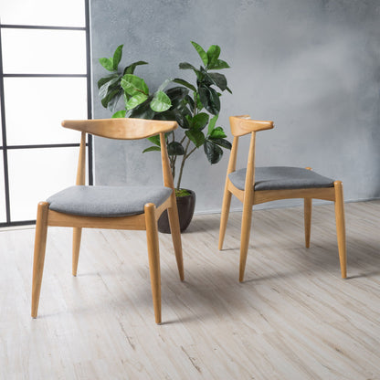 A set of two Candescent Dining Chairs with curved backs and wood frames, featuring gray cushions, sit on a light wood floor near a potted plant, against a gray textured wall and large window.