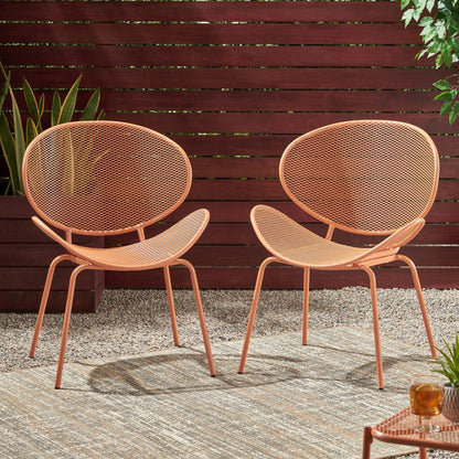 The Elba Contemporary Chair Set for Outdoor Relaxation features two modern orange metal chairs with mesh seats and backs, shown outdoors on a rug with gravel, a wooden fence, potted plants, and a small table with a drink nearby.