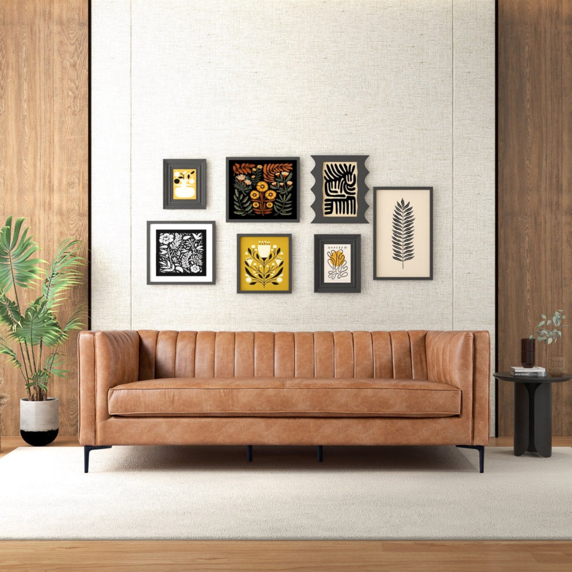 A modern living room with the Angelina Channel Tufted Sofa in light brown leather, a black side table, potted plant, and six botanical and abstract artworks on a beige wood-accented wall. A neutral rug covers the floor.
