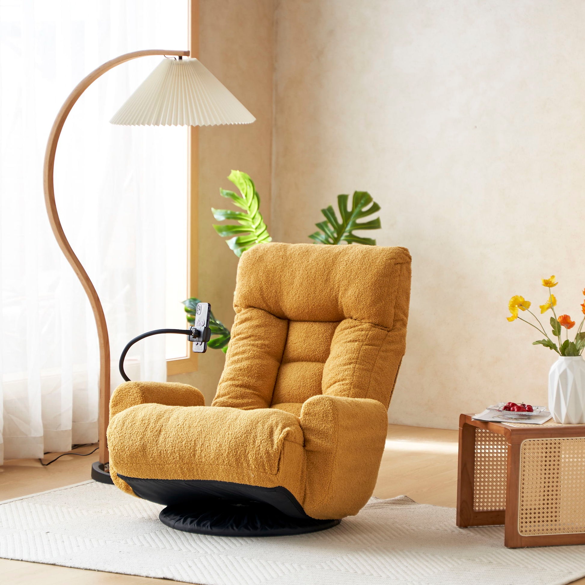 An Adjustable Swivel Lounge Chair with a 360-degree rotating seat and headrest support sits in a sunlit room by a wooden floor lamp, leafy plant, and small table topped with flowers and a bowl.