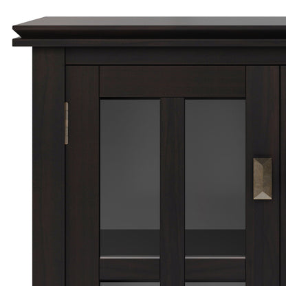 A close-up of the Couch.com Artisan Low Storage Cabinet in hickory brown shows its dark wood construction, glass-paneled door with a geometric metal handle, and an interior storage shelf.