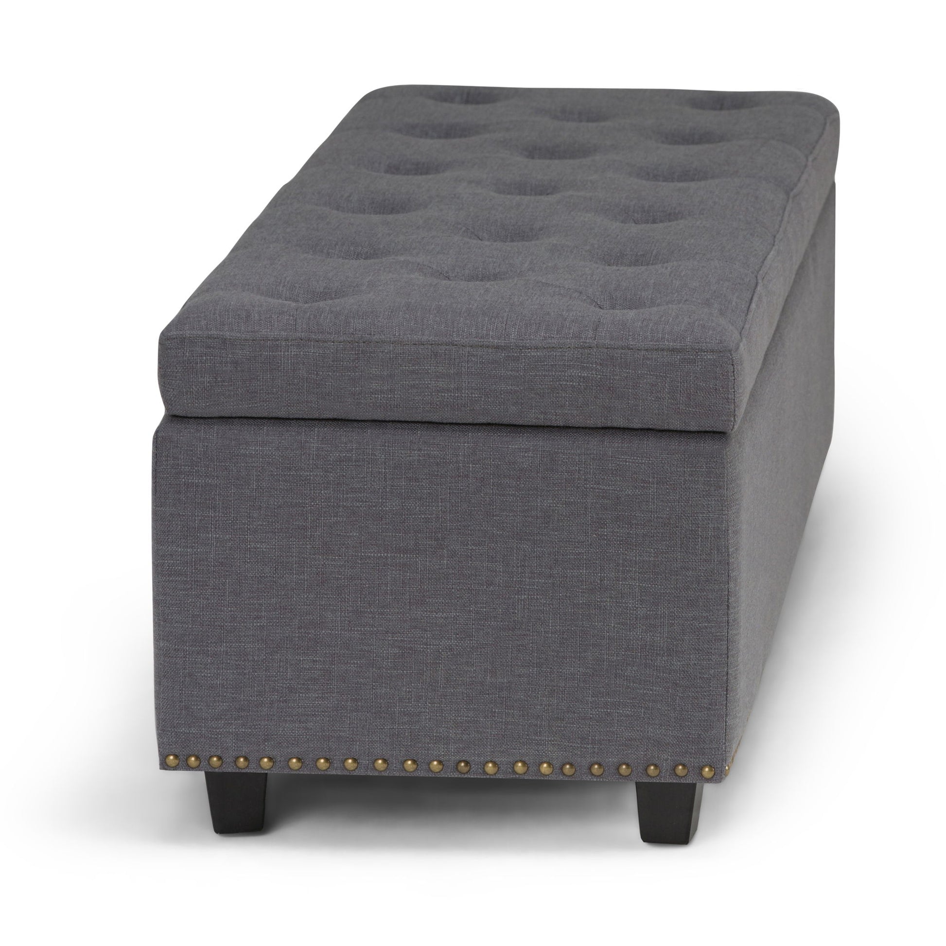 The Hamilton Upholstered Storage Ottoman features a rectangular gray design, tufted top, dark wood legs, and brass nailhead trim along the bottom edge.