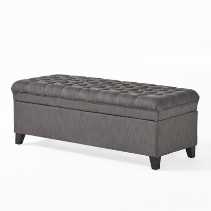 The Juliana Storage Ottoman is a rectangular gray upholstered bench with a tufted top and four short black birch legs, shown against a plain white background.
