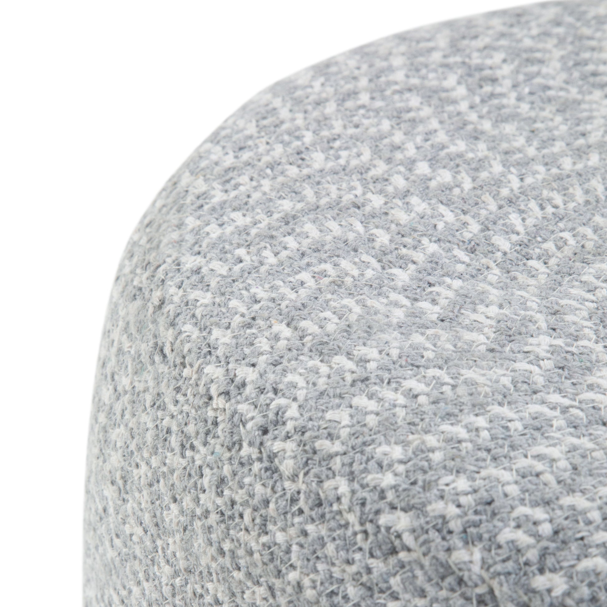 Close-up of the Bayley - Versatile Round Braided Pouf, showing its light gray textured fabric with a subtle woven pattern and curved edge, highlighting the soft upholstery material.