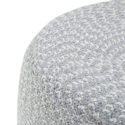 Close-up of the Bayley - Versatile Round Braided Pouf, showing its light gray textured fabric with a subtle woven pattern and curved edge, highlighting the soft upholstery material.