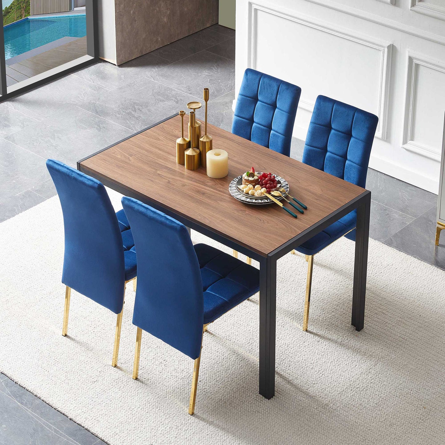The 5 Pieces Dining Set includes a creative rectangular table and four velvet high-back chairs with gold legs, arranged on a light rug in a modern room and adorned with candles, gold decor, and fruit.