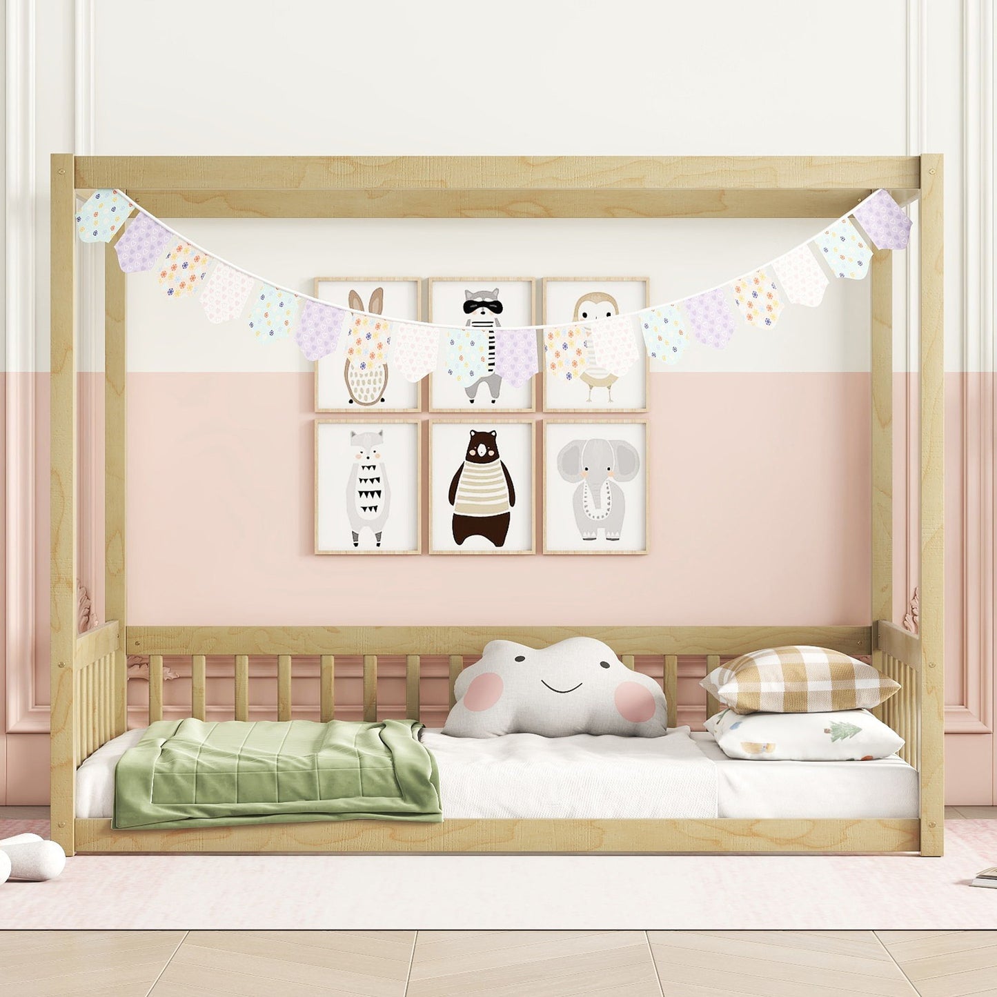 A Canopy Frame Floor Bed With Fence, Guardrails is styled with a pastel garland, animal-themed wall art, a cloud pillow, and neatly folded bedding against a two-tone pink and white wall in a cozy nursery.