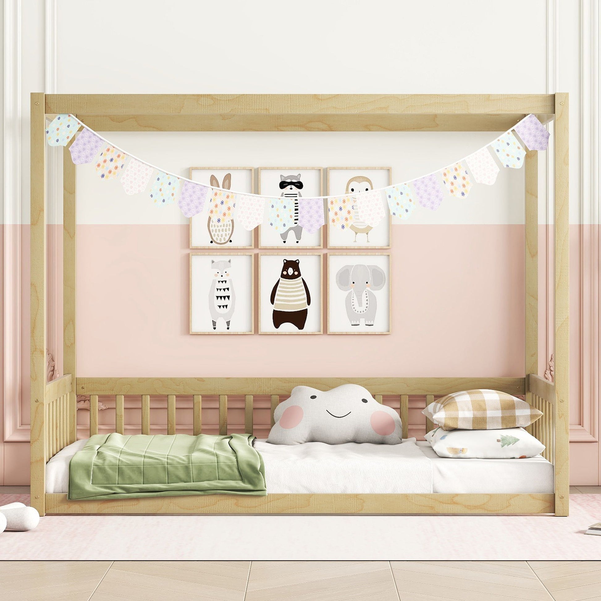 A Canopy Frame Floor Bed With Fence, Guardrails is styled with a pastel garland, animal-themed wall art, a cloud pillow, and neatly folded bedding against a two-tone pink and white wall in a cozy nursery.