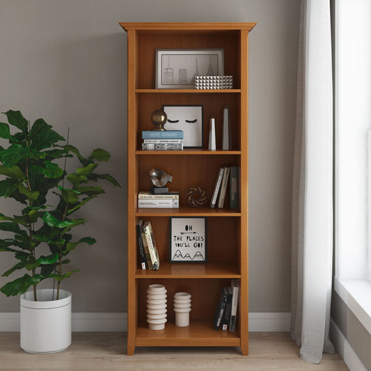 The Amherst - 5 Shelf Bookcase in Light Golden Brown displays books, art, decor, and vases. A potted plant sits to the left, while a window with white curtains on the right fills the space with light.