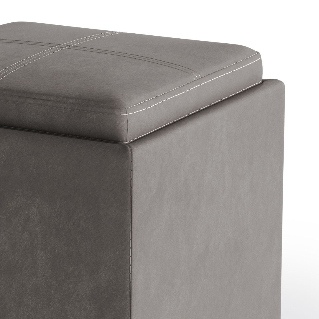Close-up of the corner of the Rockwood - Upholstered Cube Storage Ottoman With Tray, featuring a cushioned, stitched lid and visible white stitching details on the top and side.