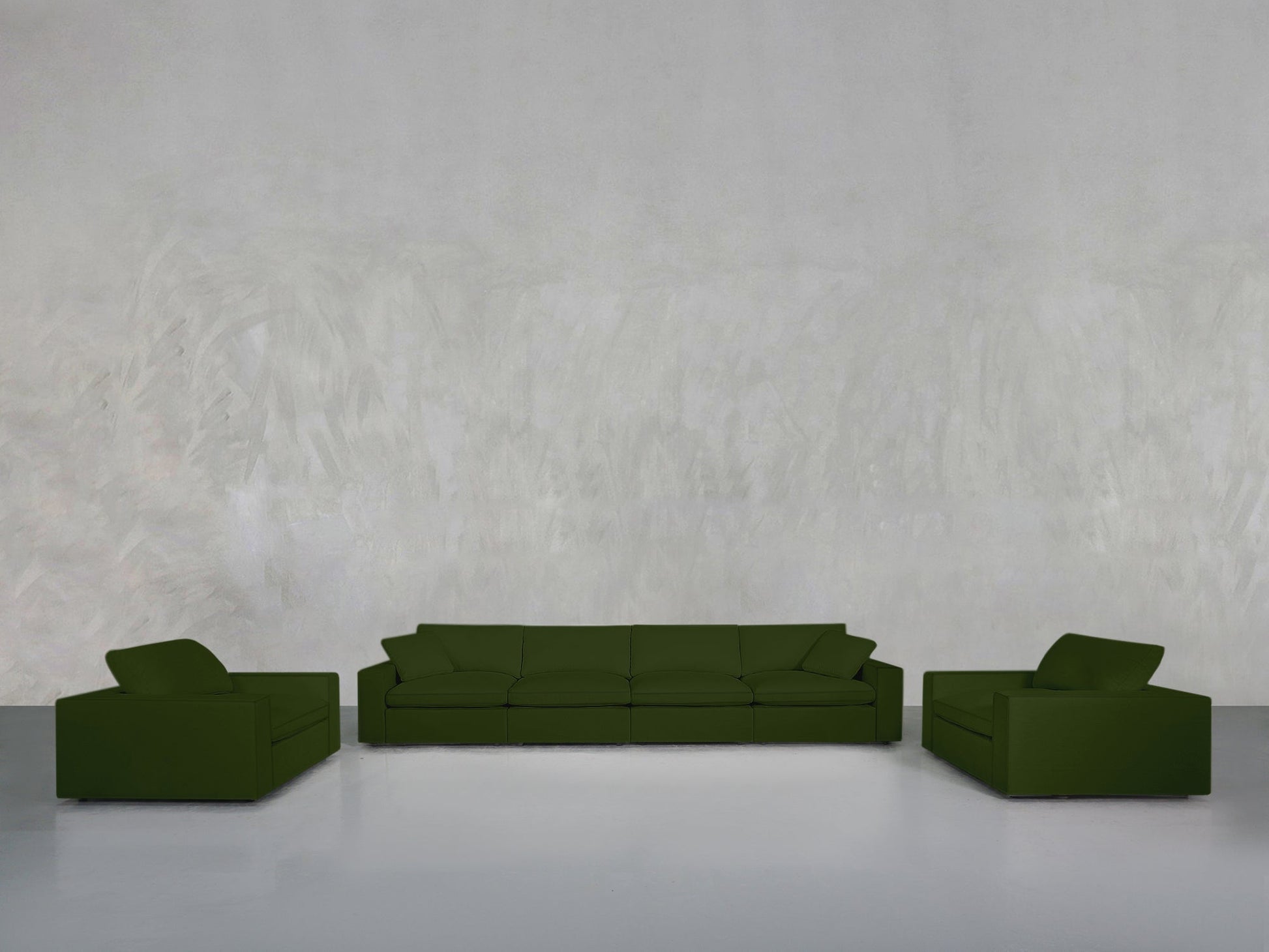 A minimalist room with a light gray textured wall showcases the 4-1-1 Sofa & Armchair Set in dark green at its center, framed by matching armchairs on a smooth light gray floor.