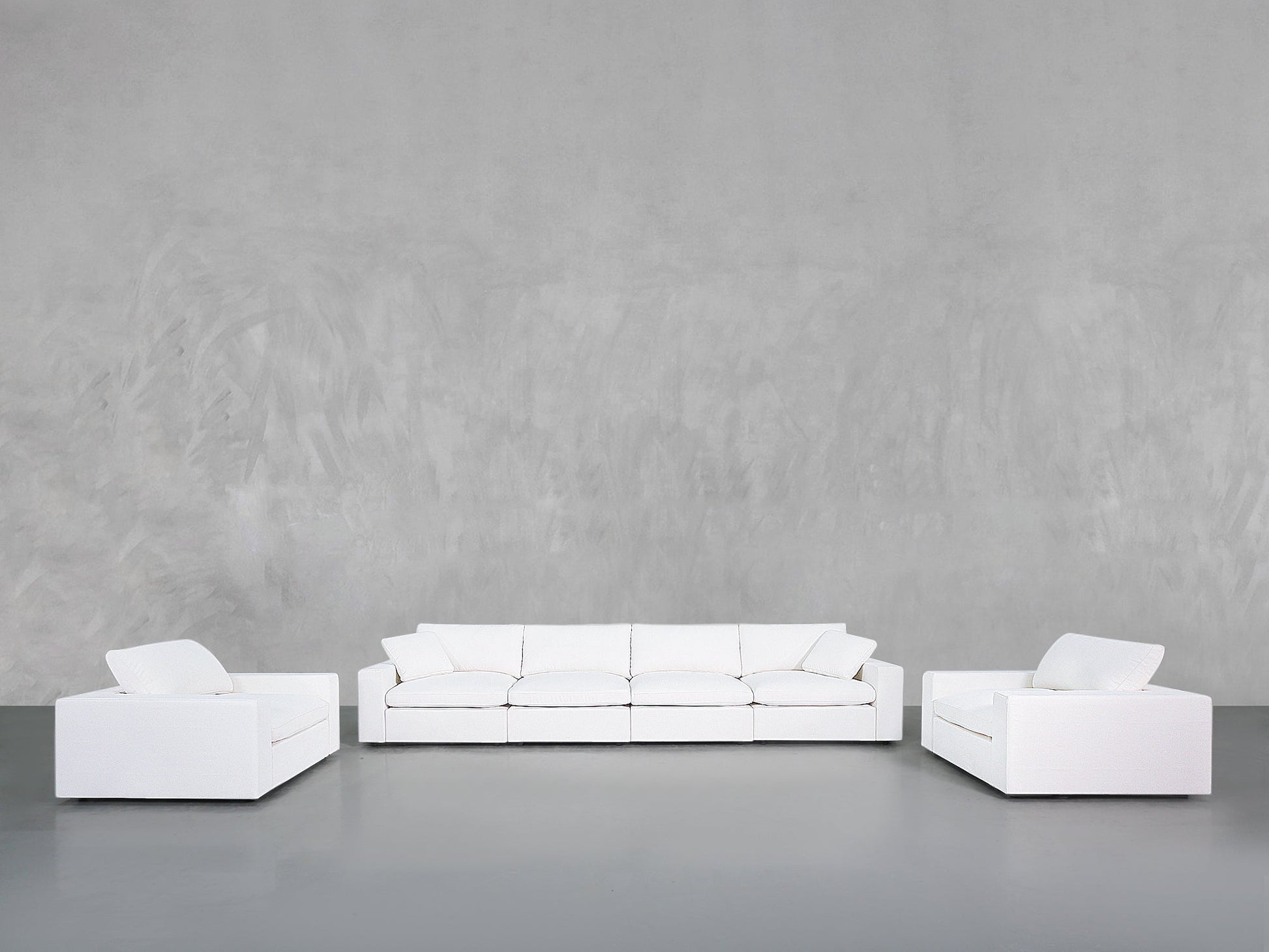 A minimalist living room showcases the 4-1-1 Sofa & Armchair Set, featuring a modern white sofa and two matching armchairs with clean lines, set against a smooth grey wall and floor.