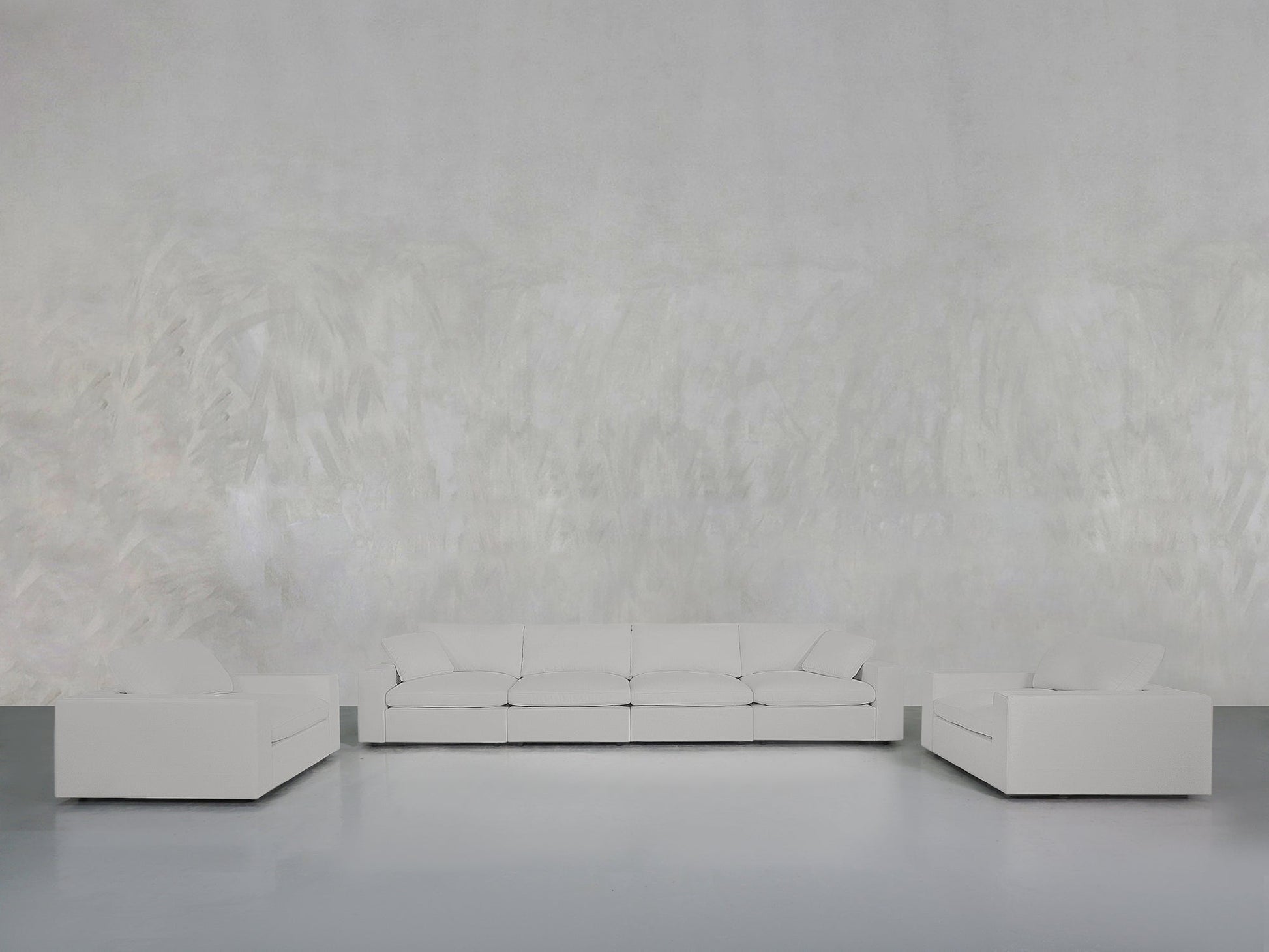 A minimalist living room with a light gray textured wall features the 4-1-1 Sofa & Armchair Set: a white three-seater sofa in the center and two matching white armchairs on either side, all placed on a smooth gray floor.