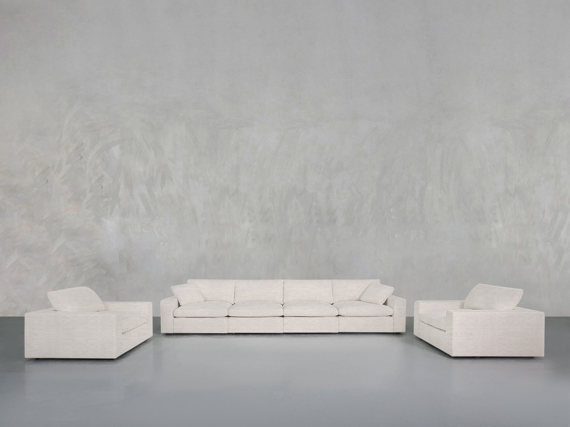 The 4-1-1 Sofa & Armchair Set, featuring a central three-seater and two single armchairs in light grey upholstery, is arranged against a minimalist grey textured wall and floor backdrop.