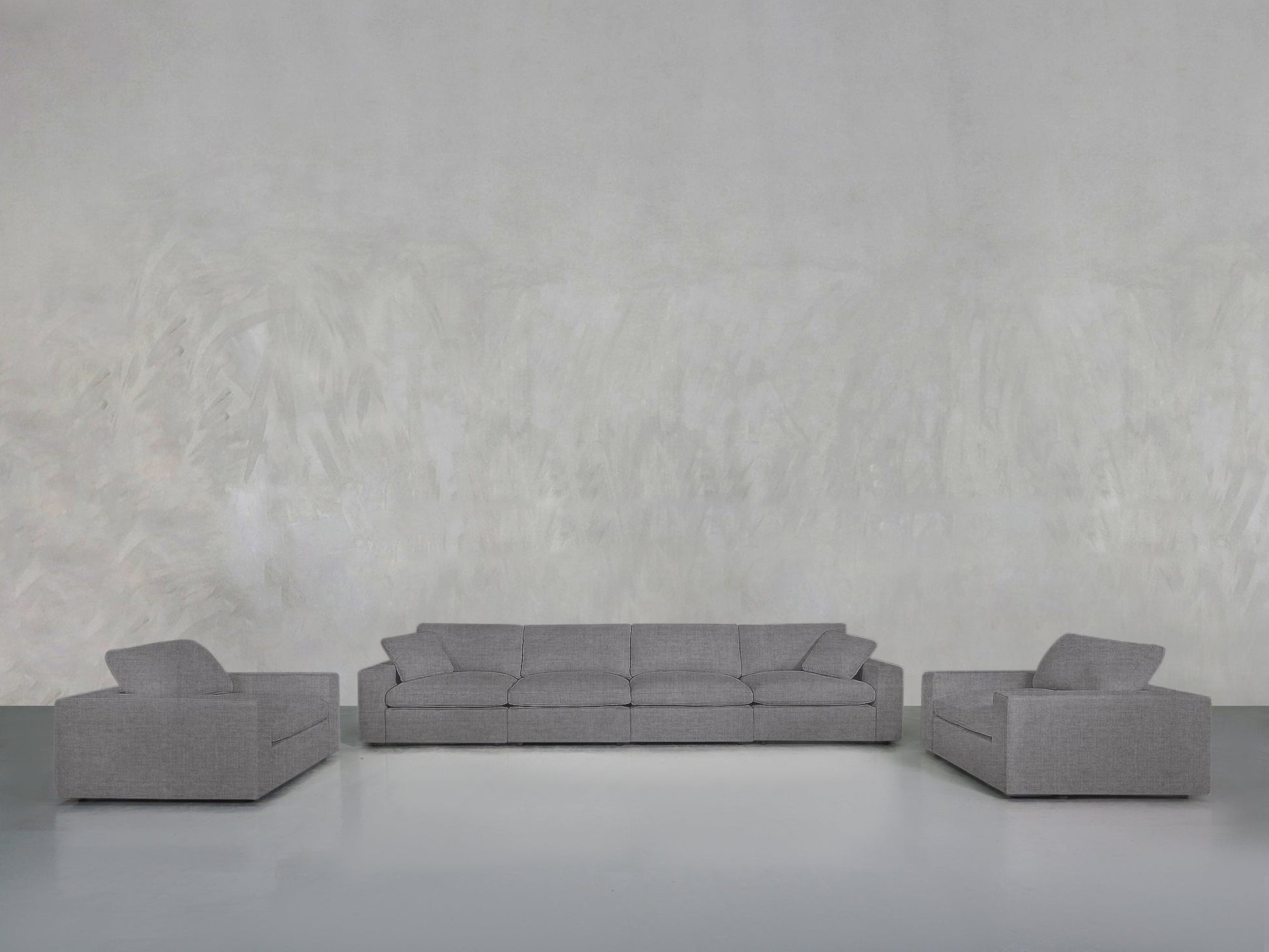 A minimalist room with a light gray textured wall, showcasing the 4-1-1 Sofa & Armchair Set: a matching gray three-seater sofa centered and two gray armchairs symmetrically placed on either side.