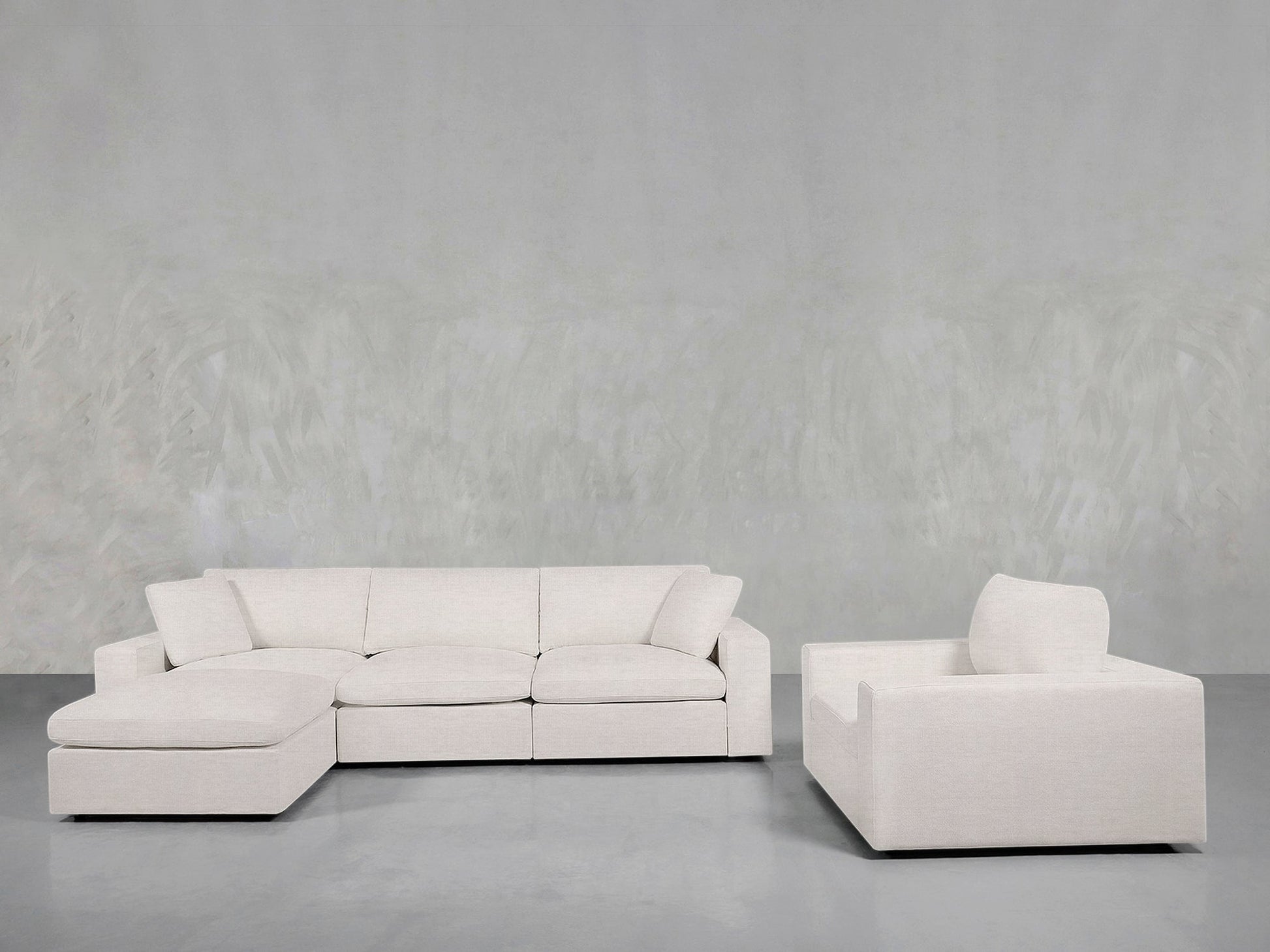 The 4-1 Sectional & Armchair Set features a light beige sectional and matching armchair, arranged on a gray floor with a textured light gray wall backdrop for a modern living room look.