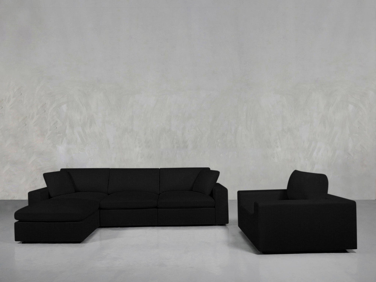 The 4-1 Sectional & Armchair Set features a dark gray sectional on the left and a matching armchair on the right, set against a light gray textured wall and smooth gray floor for a modern living room look.