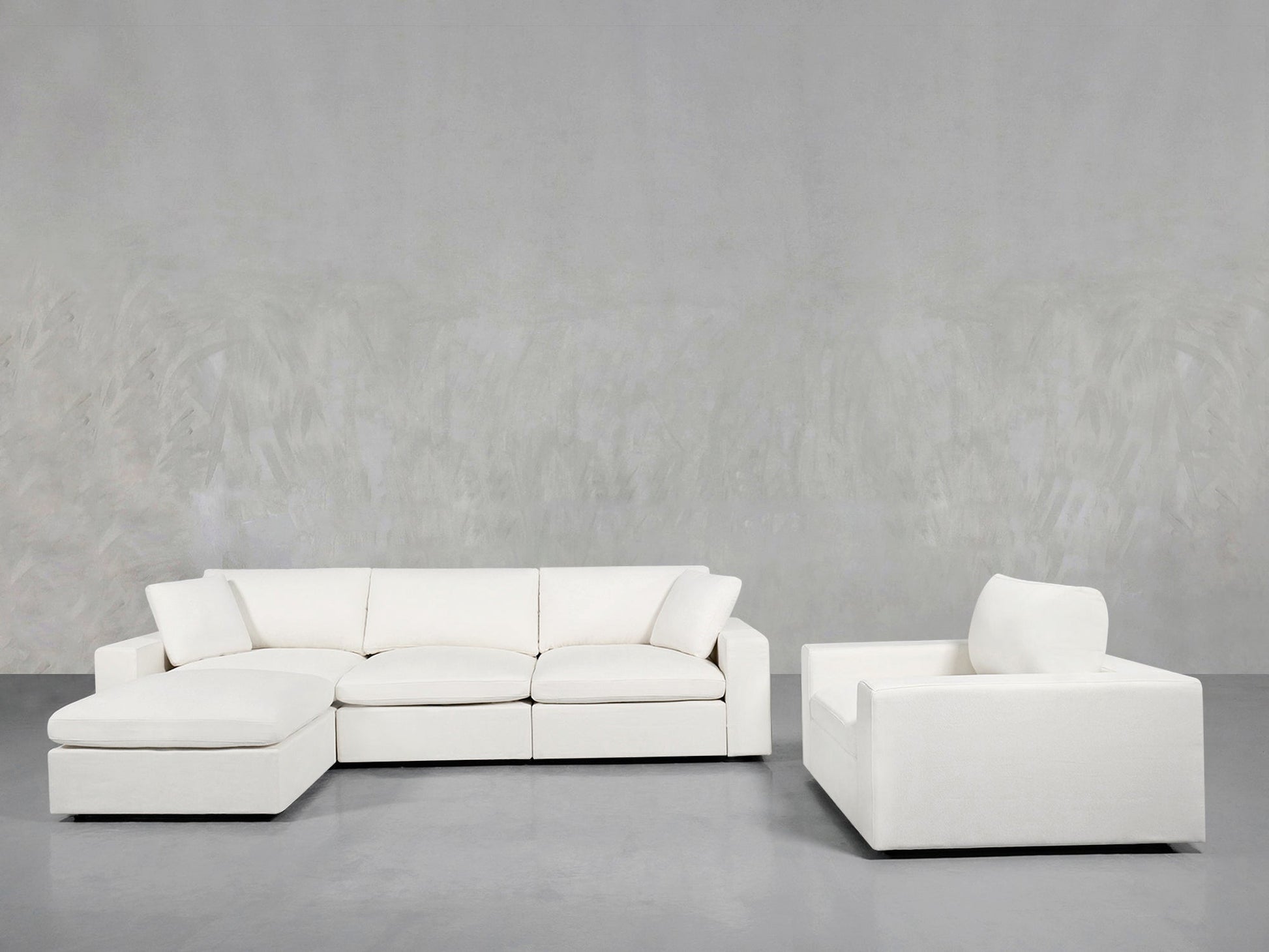 A modern minimalist living room featuring the 4-1 Sectional & Armchair Set in white, with a chaise lounge, placed against a light gray textured wall and gray floor.