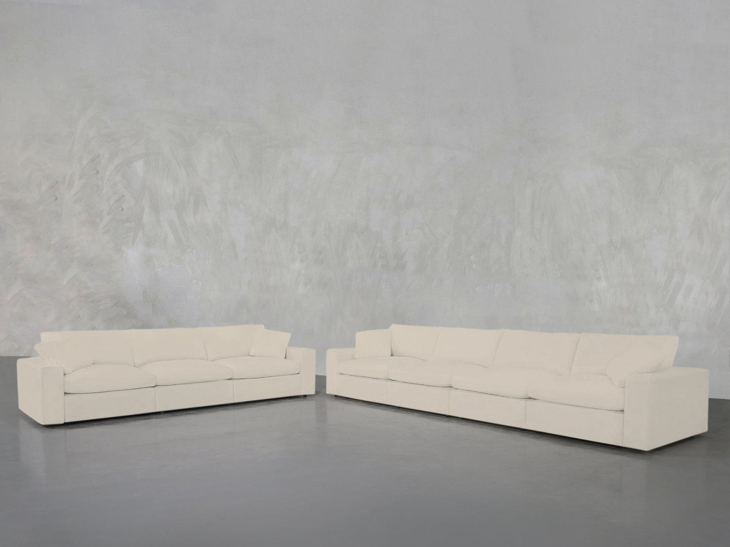 The 4-3 Sofa Set, featuring two modern light beige sofas with plush cushions, is arranged in an L-shape on a smooth grey floor against a textured light grey wall.