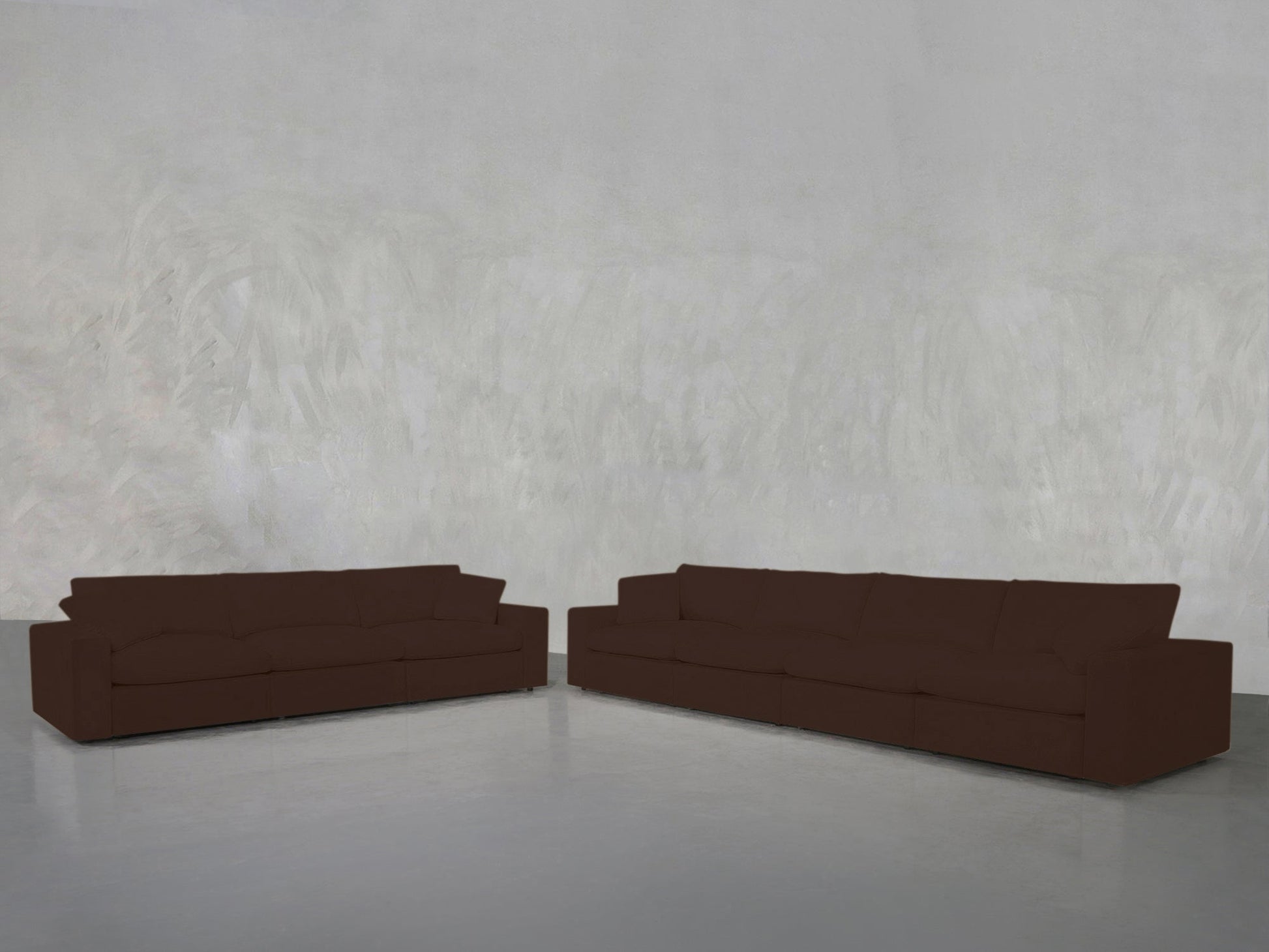 The 4-3 Sofa Set, in dark brown, is arranged in an L-shape within a minimalist room featuring light gray textured walls and a sleek gray floor.