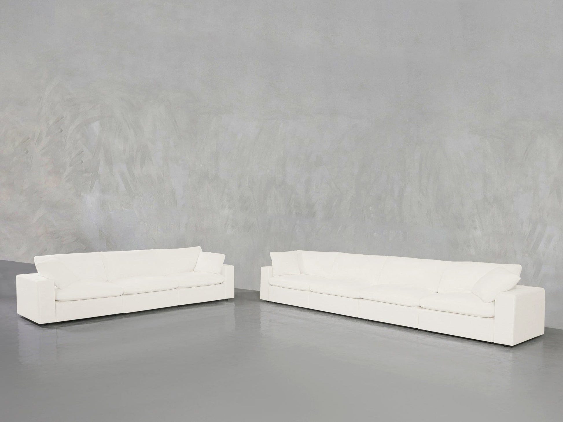 The 4-3 Sofa Set, featuring modern white boxy shapes and plush cushions, sits on a smooth gray floor against a textured light gray wall in a minimalist open space.