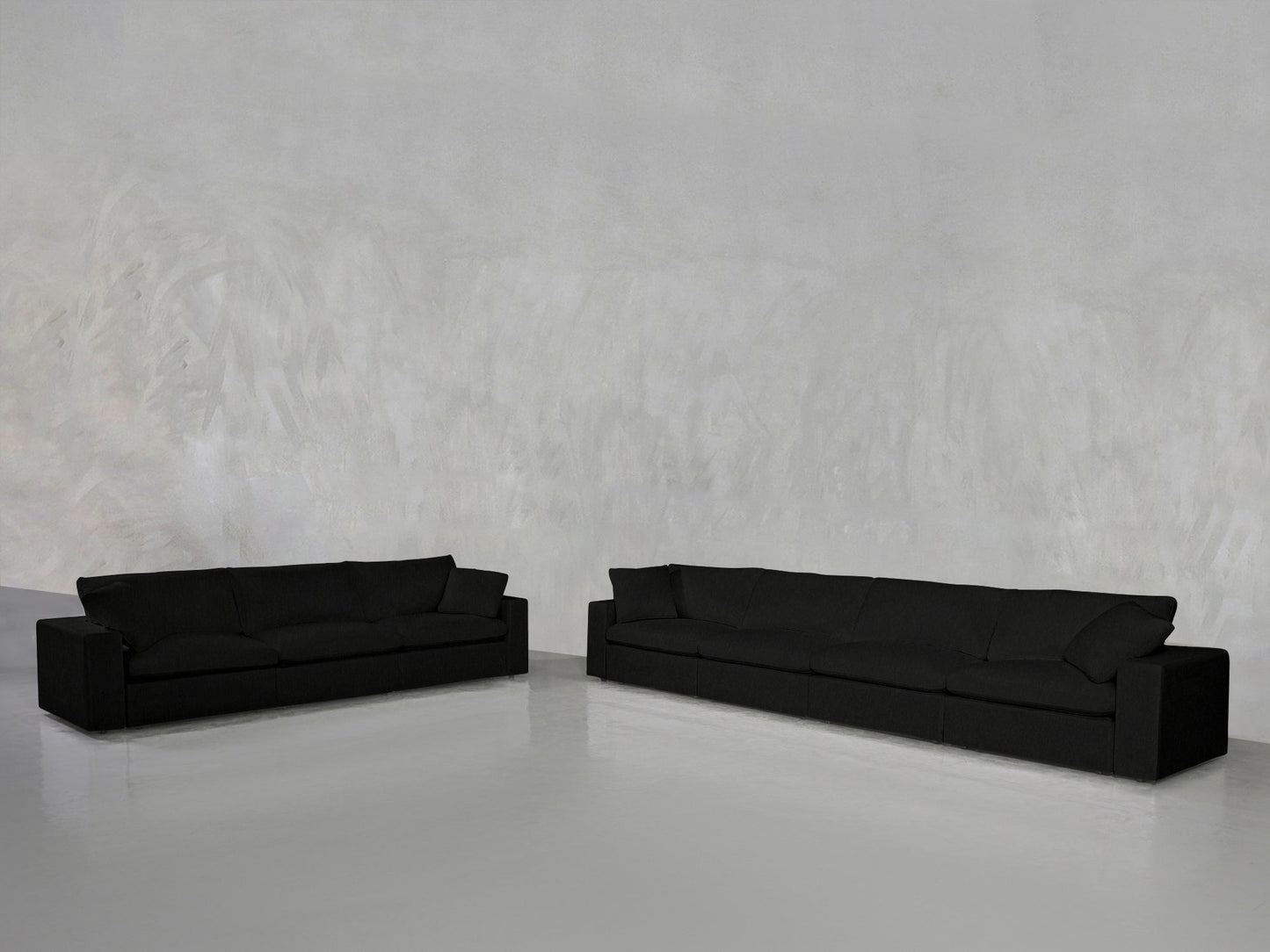 The 4-3 Sofa Set, featuring two long black sofas with clean, modern lines, sits on a shiny light gray floor against a textured pale gray wall in a minimalist, spacious room.