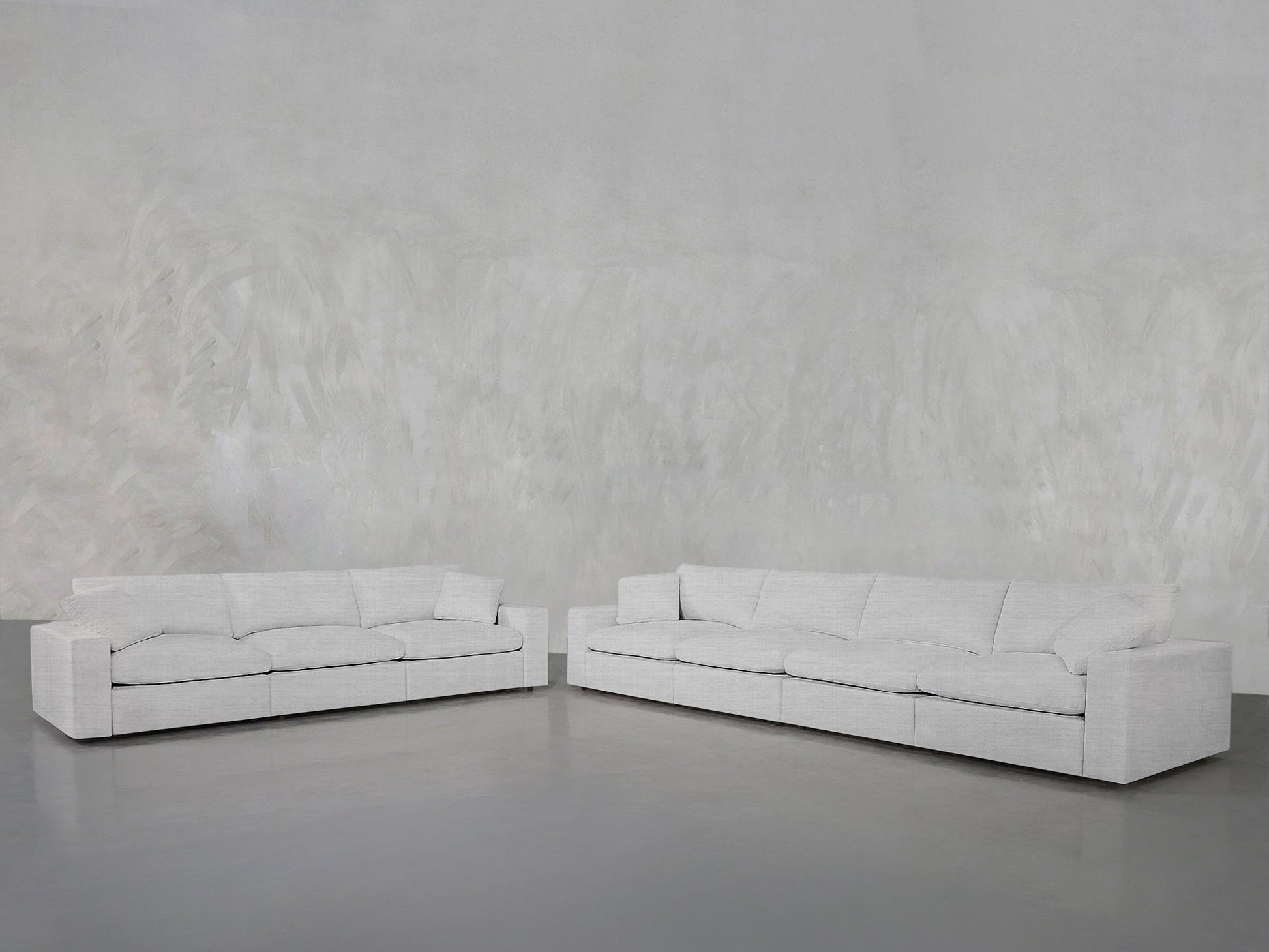 Two large, light gray 4-3 Sofa Set pieces are arranged in an L-shape against a textured, light gray wall and floor, creating a minimalist and spacious interior setting.