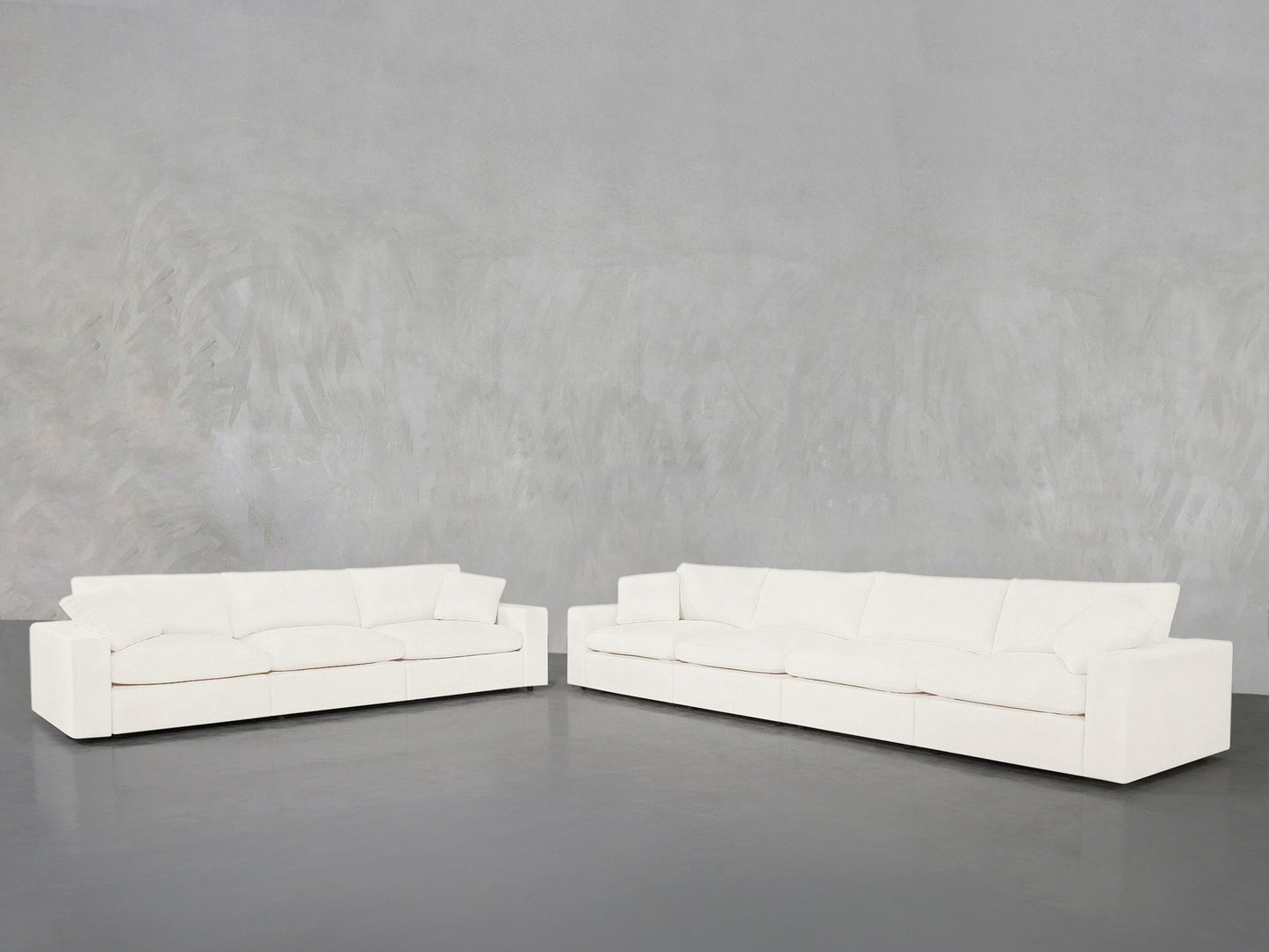 The 4-3 Sofa Set, featuring two large modern white sofas with clean lines, is arranged in an L-shape against a light gray textured wall and dark gray floor, creating a minimalist, contemporary look.