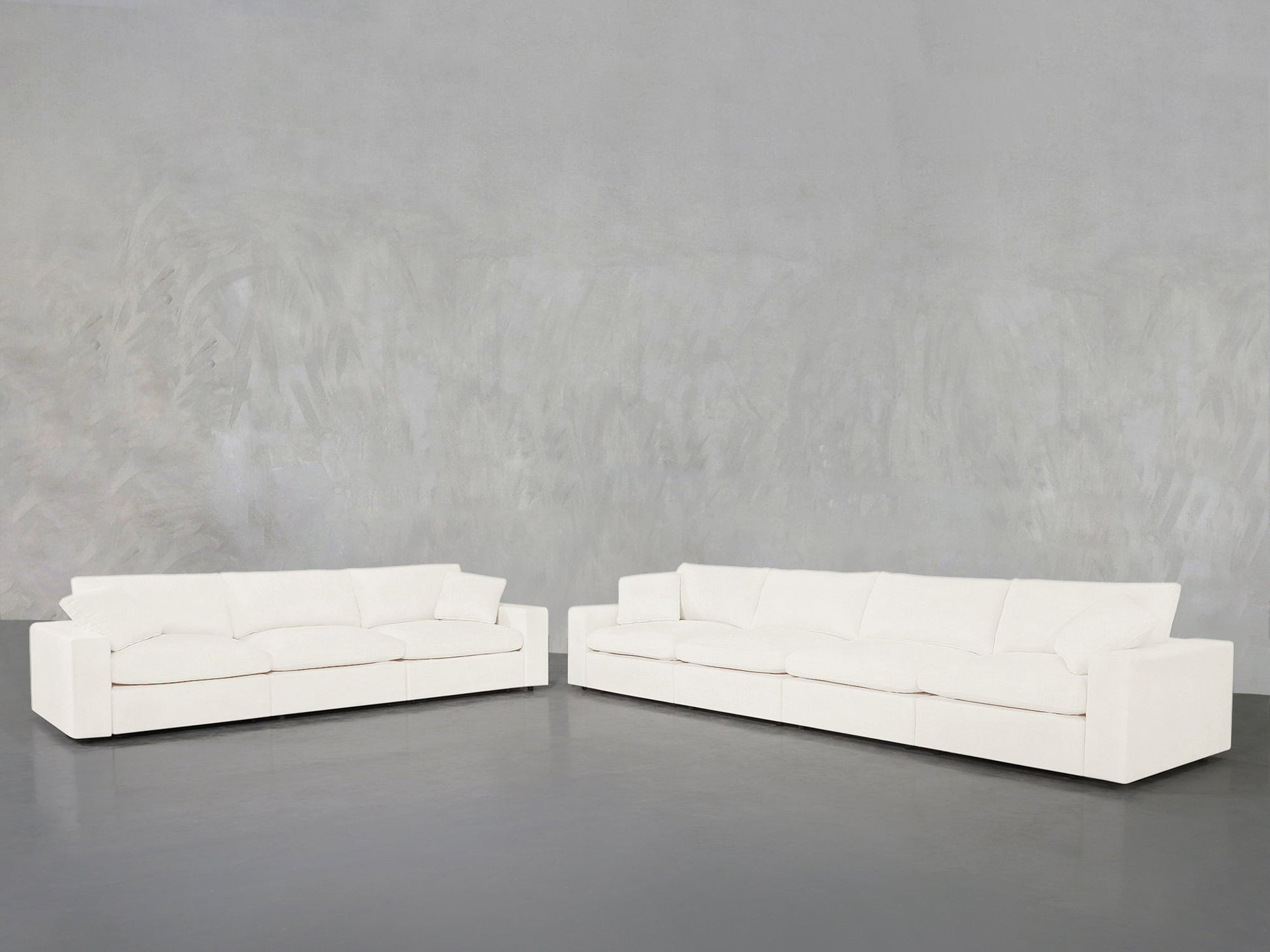 The 4-3 Sofa Set, featuring two large modern white sofas with clean lines, is arranged in an L-shape against a light gray textured wall and dark gray floor, creating a minimalist, contemporary look.