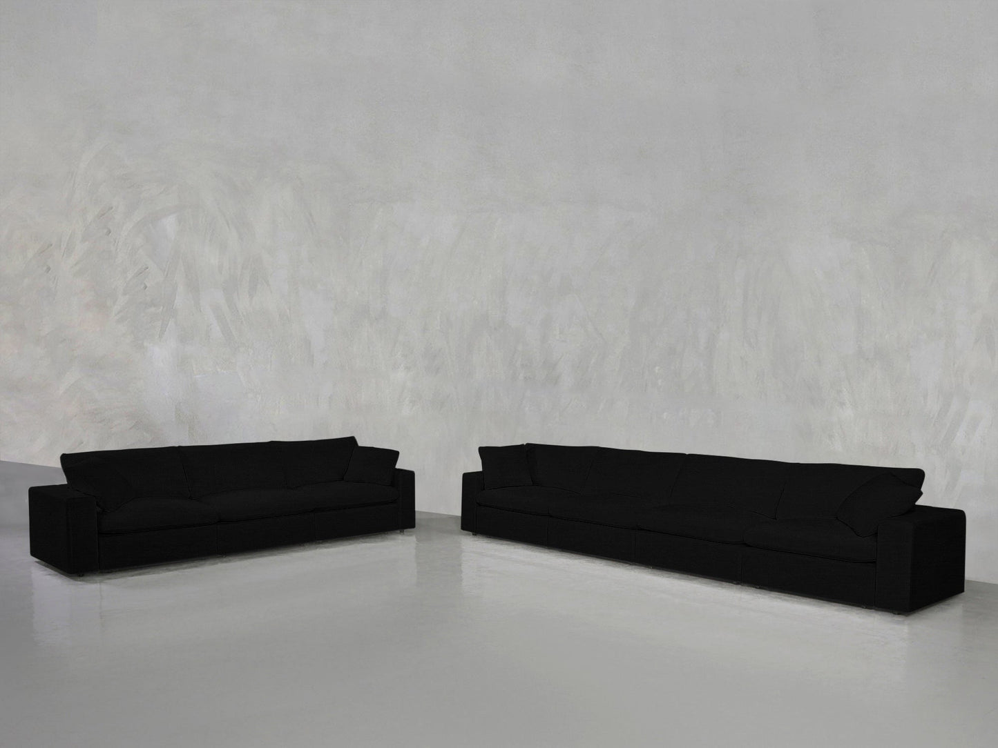 The 4-3 Sofa Set, featuring two black sofas of varying lengths, is arranged on a polished light gray floor against a textured light gray wall in a minimalist setting.