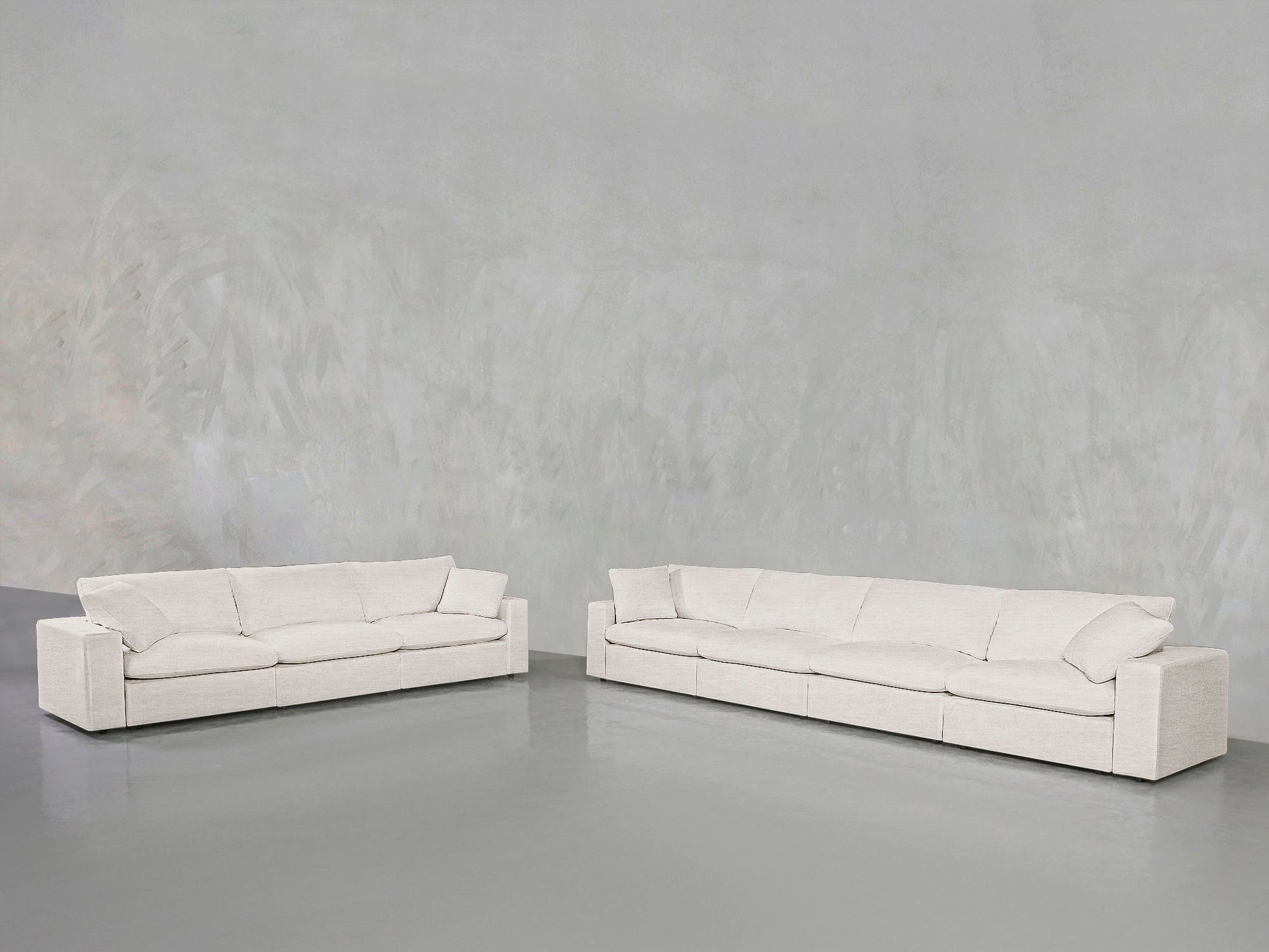 The 4-3 Sofa Set, featuring two modern off-white sofas with clean lines, is arranged in a minimalist room with a light gray textured wall and a smooth gray floor.