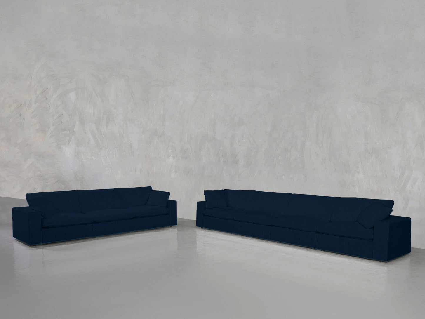 The 4-3 Sofa Set in navy blue sits on a shiny light gray floor against a textured light gray wall, creating an open, minimal space that emphasizes the sofas’ clean lines.