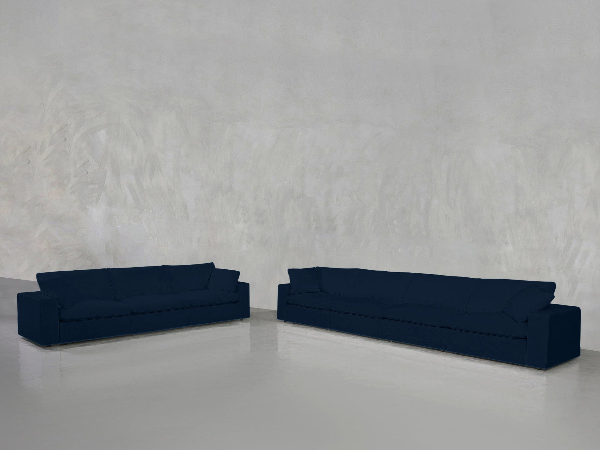 The 4-3 Sofa Set in navy blue sits on a shiny light gray floor against a textured light gray wall, creating an open, minimal space that emphasizes the sofas’ clean lines.