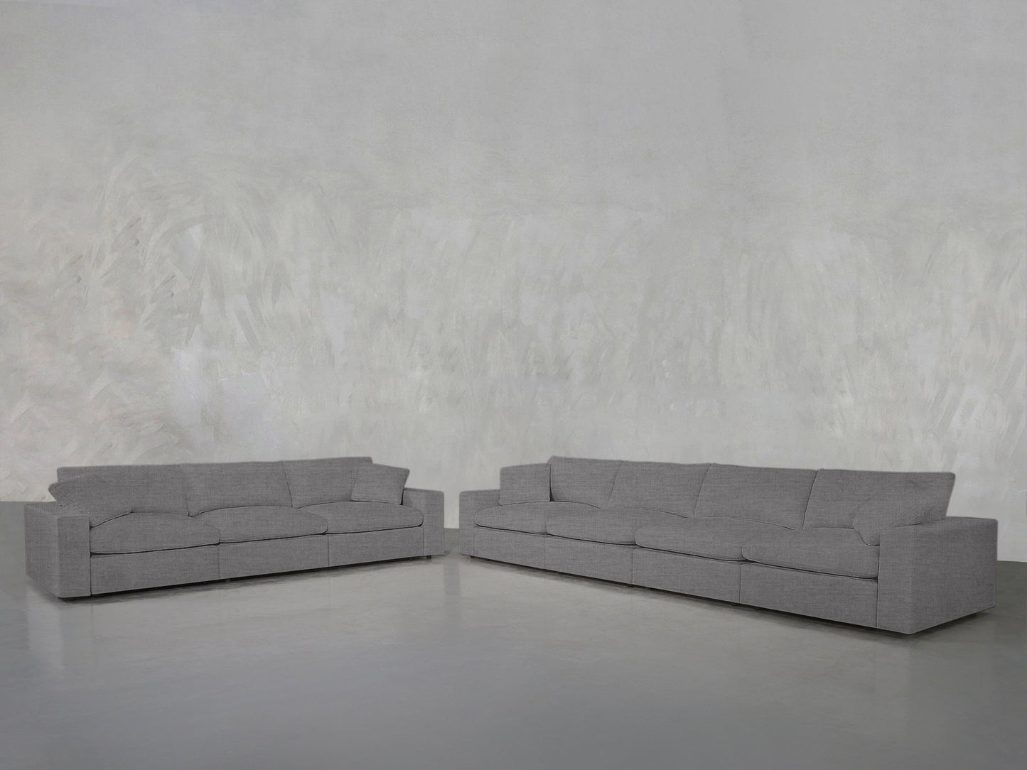 The 4-3 Sofa Set, featuring modern gray upholstery and straight lines, is arranged in an L-shape against a light gray textured wall on a smooth, light-colored floor.