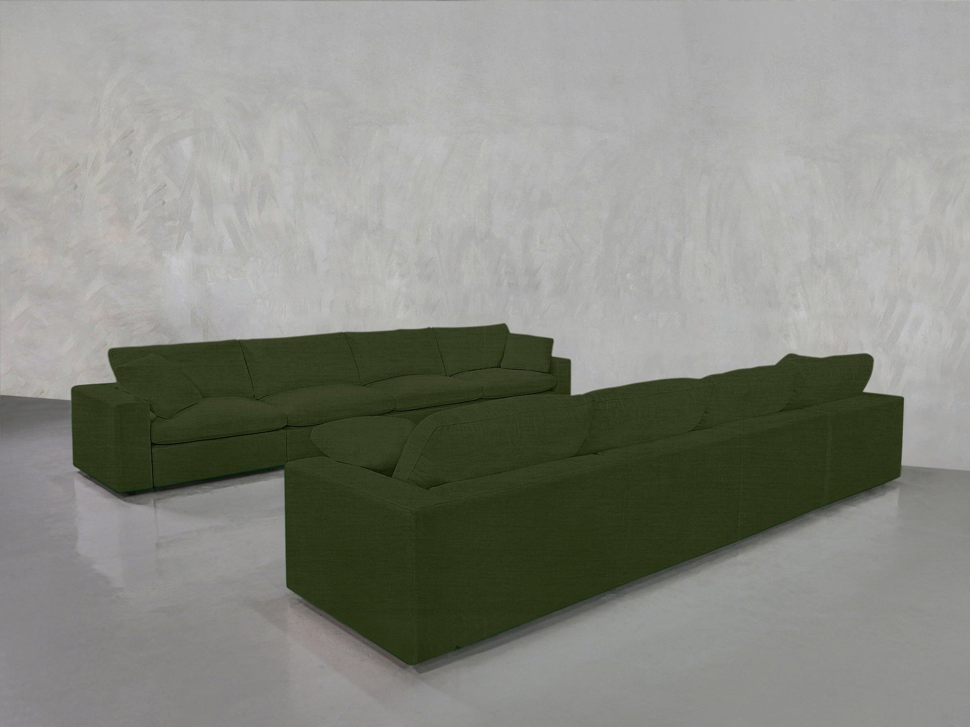 The 4-4 Sofa Set, featuring two large modern dark green sofas in an L-shape, complements the minimalistic room with light gray textured walls and a shiny gray floor.